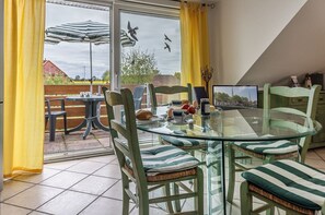 Un comedor con mesa de vidrio, sillas con cojines a rayas y vista a través de un ventanal.