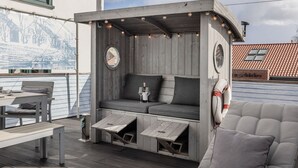 Ein gemütlicher Sitzbereich im Freien mit Holzkonstruktion, gepolsterten Sitzgelegenheiten und einem Tisch mit Flasche und Gläsern.