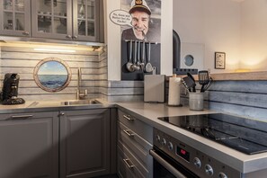 Une cuisine moderne dotée d’un four encastré, d’une machine à café et d’une grande fenêtre offrant une vue sur la mer.