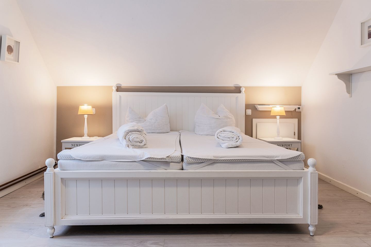 Una cama doble con ropa de cama blanca, dos mesitas de noche con lámparas y un cabecero blanco.