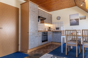 A compact kitchen with a stove, oven, microwave, and a dining area with chairs and a table.