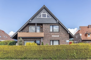 A two-story house with a prominent triangular roof, a balcony, and a well-maintained hedge in the foreground.