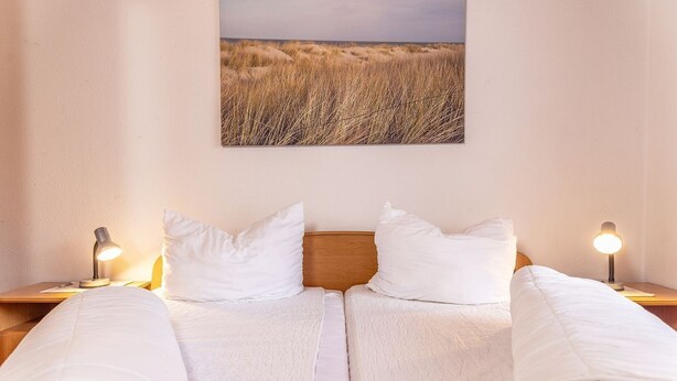 Un letto matrimoniale con biancheria bianca, due lampade ai comodini e un quadro con un paesaggio appeso al muro.