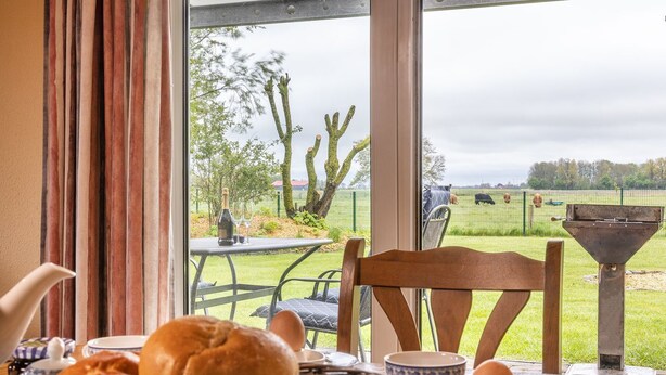 A breakfast table with bread, eggs, and a bottle of wine, overlooking a grassy area with trees and a fence.
