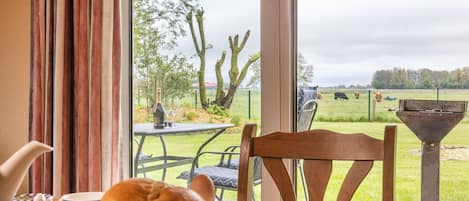 A breakfast table with bread, eggs, and a bottle of wine, overlooking a grassy area with trees and a fence.