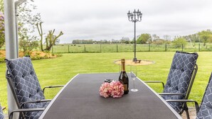An outdoor patio with a table, chairs, a bottle of champagne, and a glass.