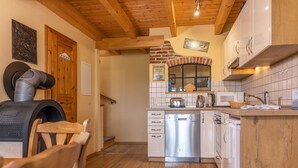 A kitchen with a brick oven, stainless steel dishwasher, wooden cabinets, and a wooden ceiling.