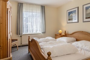 Habitación de hotel con cama de madera, mesita de noche con lámpara, silla de mimbre y ventana con cortinas.