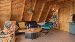 Un acogedor cuarto estilo loft con techo de madera, un sofá de cuero negro, un sillón verde, una mesa de centro de madera y una estantería llena de libros.