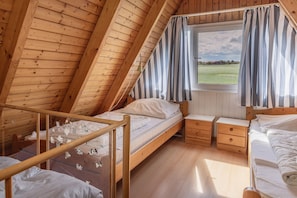 Une chambre mansardée chaleureuse avec un plafond en pente en bois, un lit simple, une petite table de chevet et une fenêtre avec des rideaux.
