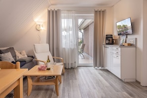 Una sala de estar acogedora con un sofá, una mesa de madera y una zona de cocina con cafetera.