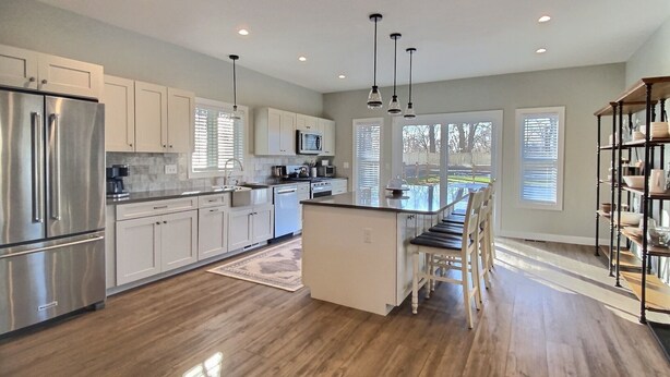 A modern kitchen with stainless steel appliances, white cabinetry, and a central island with bar stools. - Hilltop House (Litchfield)