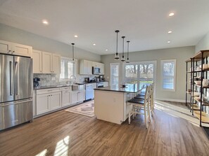 A modern kitchen with stainless steel appliances, white cabinetry, and a central island with bar stools. - Hilltop House (Litchfield)
