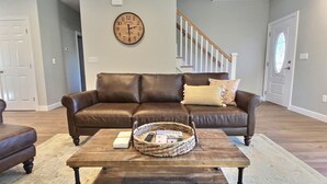 A living room with a brown leather sofa, a wooden coffee table, and a wicker basket. - Hilltop House (Litchfield)
