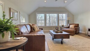 A spacious living room with a brown leather sofa, a smaller sofa, a coffee table, and a ceiling fan. - Hilltop House (Litchfield)