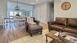 A spacious living room with a brown leather sofa, a wooden coffee table, and a dining area with a white table and chairs. - Hilltop House (Litchfield)
