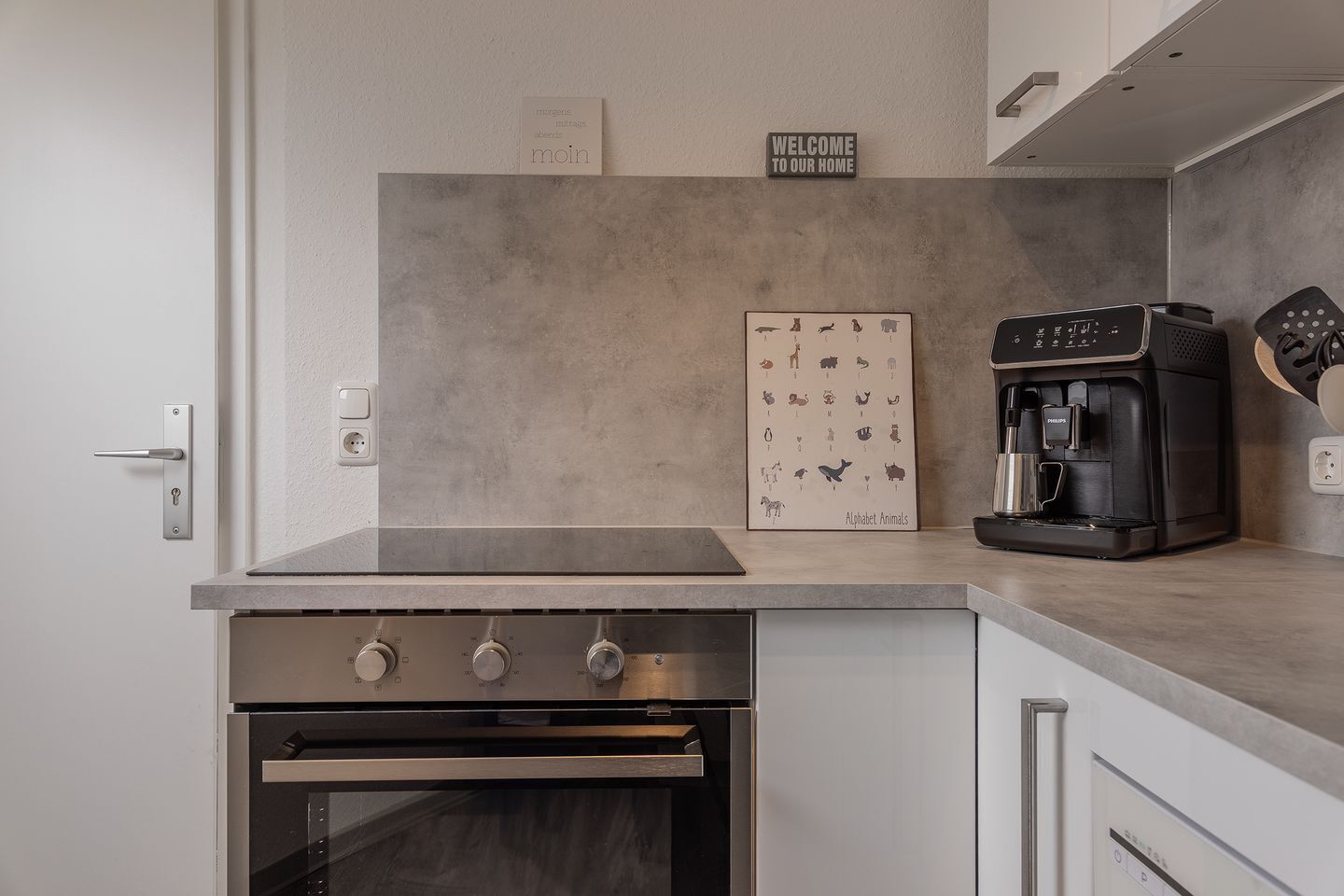 A modern kitchen with a built-in oven, a coffee machine, and a welcome sign.