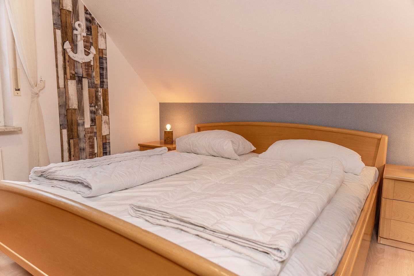 A neatly made bed with white linens, a wooden headboard, and a bedside table with a lamp.