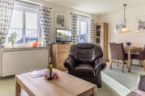 A cozy living room with a leather armchair, wooden dining table, and a TV on a cabinet.