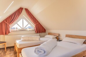 Ein Schlafzimmer mit zwei Betten, einem Fenster mit Vorhängen, einem Heizkörper und einem Holzboden.