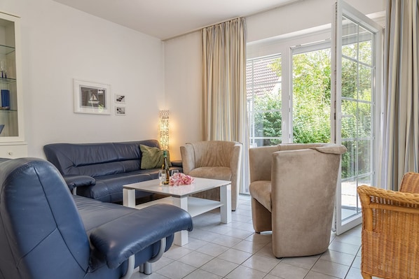 Een moderne woonkamer met een blauwe bank, beige fauteuils, een witte salontafel en een rieten stoel.