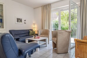 En moderne stue med blå sofa, beige lænestole, et hvidt sofabord og en fletstol.