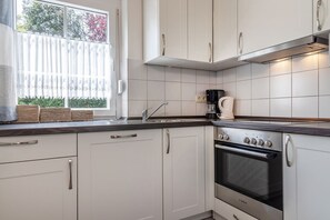 Keittiössä on valkoiset kaapit, Bosch-merkkinen uuni, kahvinkeitin ja ikkuna, josta avautuu näkymä vehreään maisemaan.