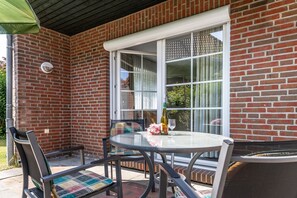 A patio with a round table and chairs, a bottle of wine, and a glass on the table.
