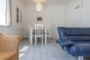 Et værelse med et spisebord og stole, en blå lædersofa og en fletstol.