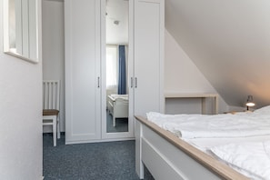 Een slaapkamer met een bed, een stoel, een kledingkast en een bureau met een lamp.