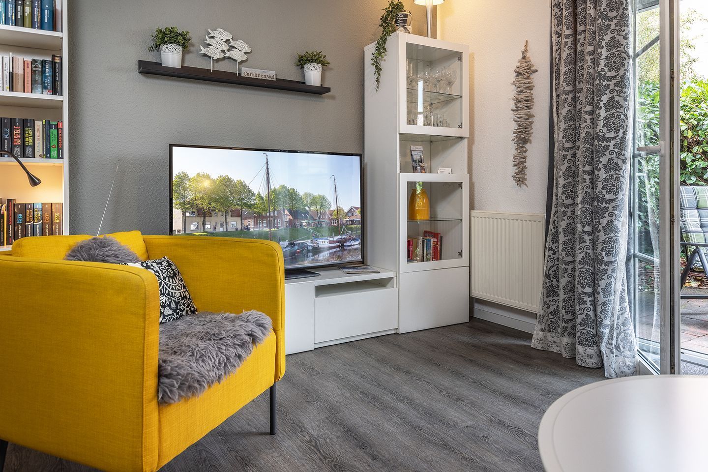 Een moderne woonkamer met een geel sofa, een flatscreen televisie, een witte kast en uitzicht op een gracht.