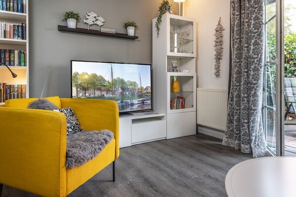 Una sala de estar moderna con un sofá amarillo, un televisor de pantalla plana, un mueble blanco y vistas a un canal.