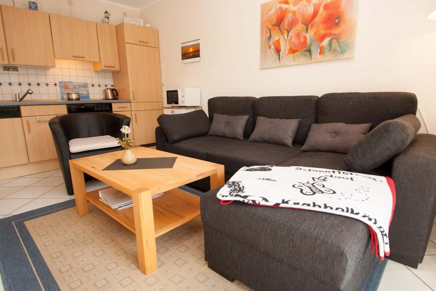 Ein kompakter Wohnraum mit einer Couch, einem kleinen Tisch, einer Küchenzeile und einem Bild an der Wand.