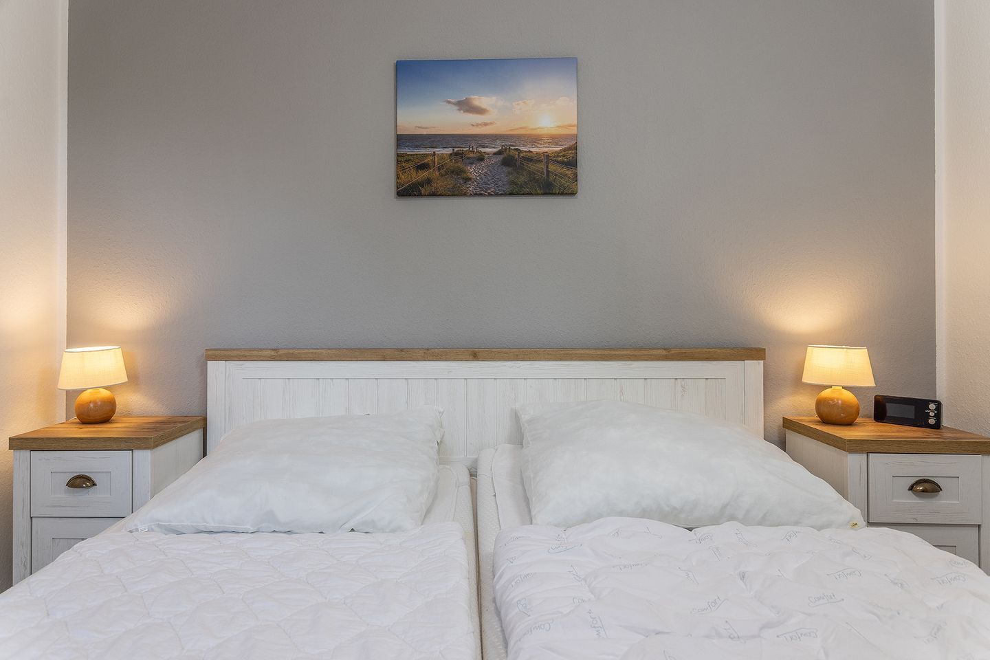 Un letto matrimoniale con biancheria bianca, due comodini con lampade, un quadro appeso al muro e una testiera in legno.