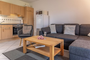 A compact living space with a kitchenette, a sofa, a coffee table, and a chair. - Vacation Apartment 50166 - A Cozy Getaway for 2: The first-floor apartment is (Wittmund)