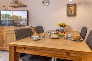A dining table with chairs, a television, a clock, and a decorative wall piece. - Vacation Apartment 50166 - A Cozy Getaway for 2: The first-floor apartment is (Wittmund)