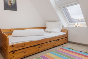A wooden bed with white bedding in a room with a skylight and a colorful striped rug.