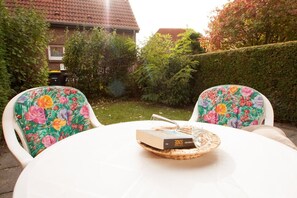 An outdoor dining area with a white table and two chairs with floral upholstery.