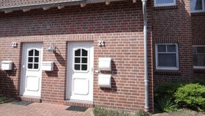 Ein zweistöckiges Backsteingebäude mit zwei weißen Türen, jeweils mit einem kleinen Fenster darüber. Im oberen Stock befinden sich zwei kleine Fenster und auf der rechten Seite des Gebäudes ein weiteres Fenster.
