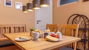 Ein Esstisch mit Stühlen, einer Kaffeemaschine, einer Obstschale und einem Käseplatte.