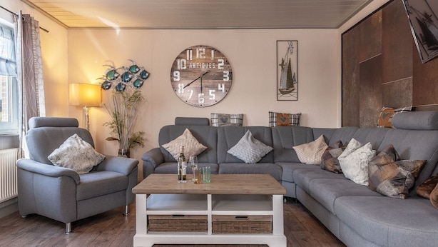 Ein Wohnzimmer mit Sofa, Sessel, Couchtisch und Dekoration, darunter eine Uhr und Wandbilder.