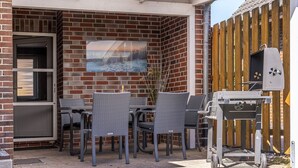 Eine Terrasse mit Korbstühlen, einem Grill und einem großen Fenster.