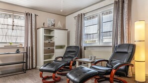 Ein Zimmer mit zwei Ledersesseln, einem kleinen Tisch mit zwei Tassen, einem Bücherregal und einer Heizung.