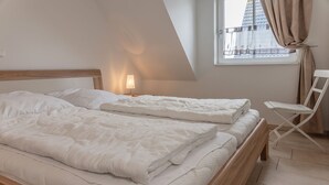 Une chambre avec deux lits, une table de chevet, une lampe, une chaise et une fenêtre avec des rideaux.
