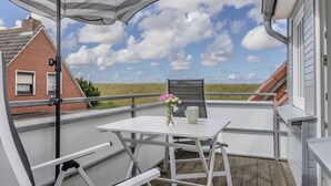 Un balcon avec une table blanche, une chaise en métal et un parasol à rayures.