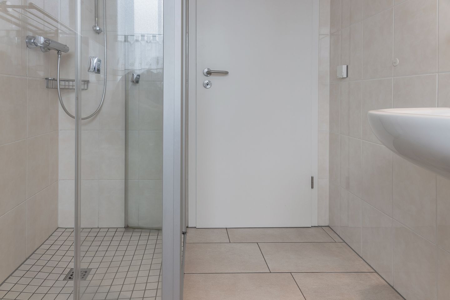Une salle de bain avec une douche à parois de verre, un lavabo blanc et un carrelage au sol.