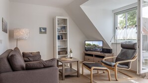 Un salon moderne comprenant un canapé, une table basse, une bibliothèque, un téléviseur et un fauteuil.