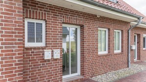 Un bâtiment en briques avec un toit recouvert de tuiles rouges, une porte en verre et deux fenêtres.