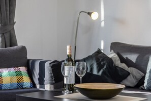Un salon moderne avec un canapé, une bouteille de vin et deux verres posés sur une table.