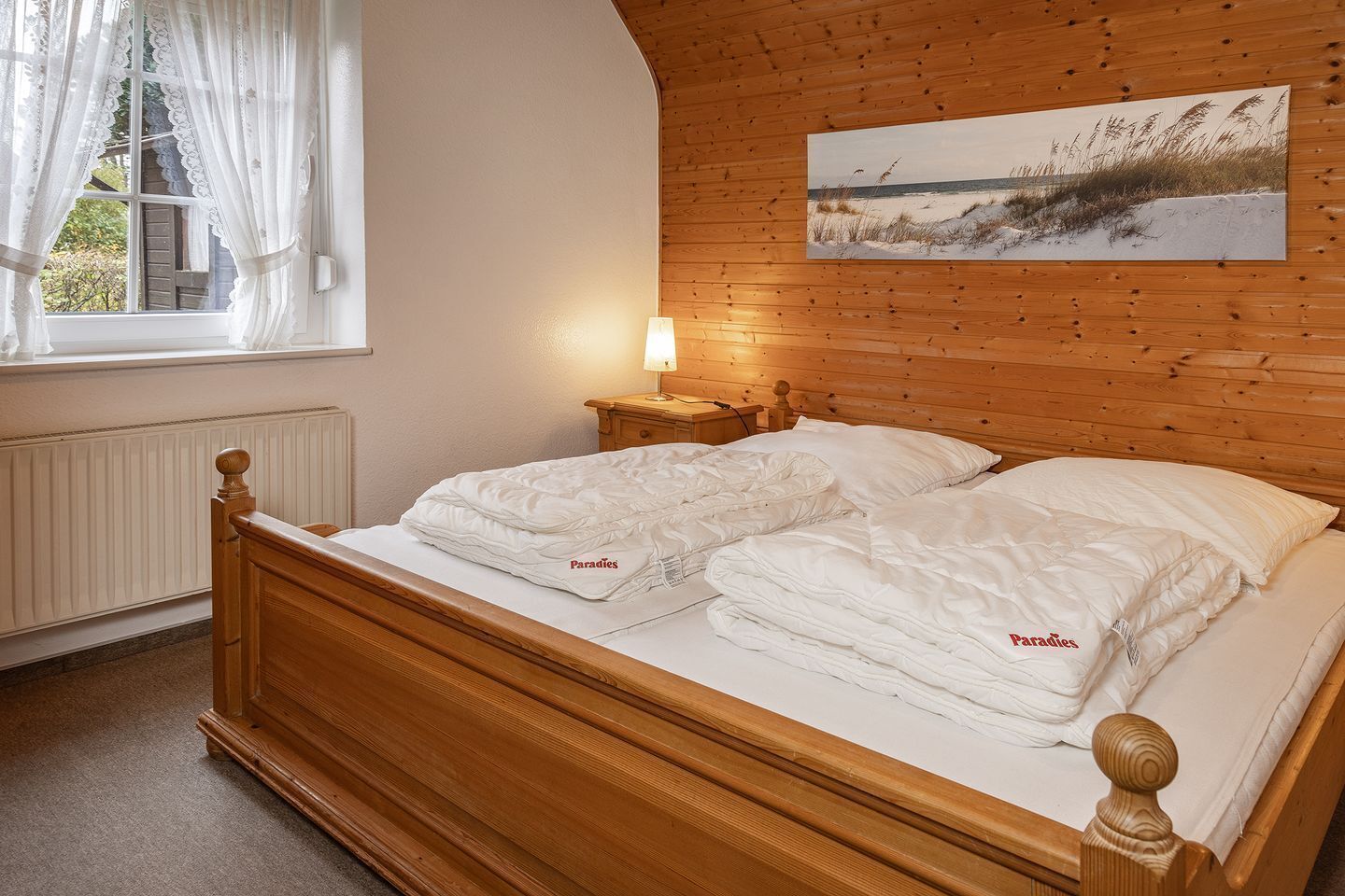 Een houten bed met wit beddengoed en een lamp op een nachtkastje.